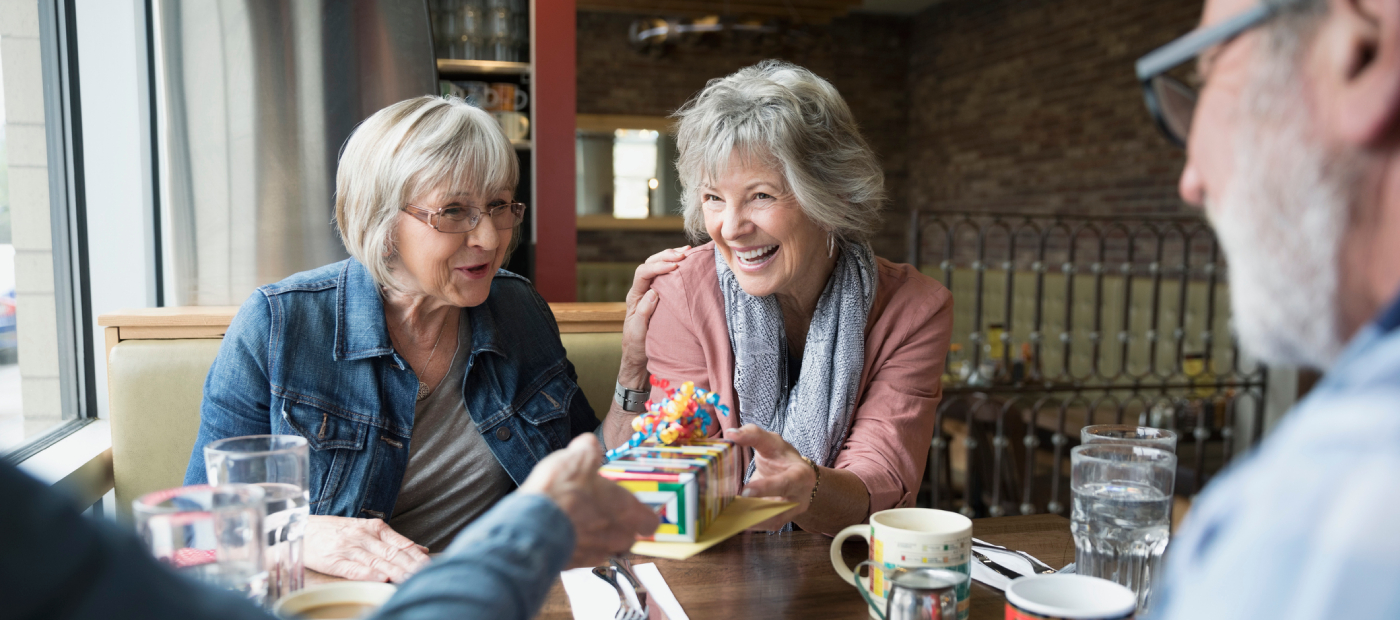 Smiling senior woman receiving birthday gift from friend in diner booth